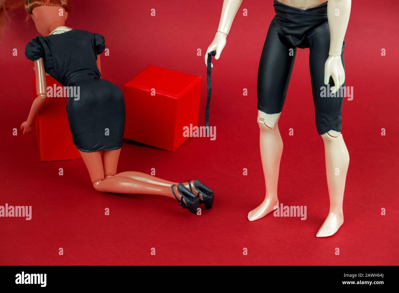 hombre sosteniendo un látigo y una mujer en un vestido de cuero negro sobre un fondo rojo, una vida creativa con el concepto sexual de las muñecas plásticas Foto de stock