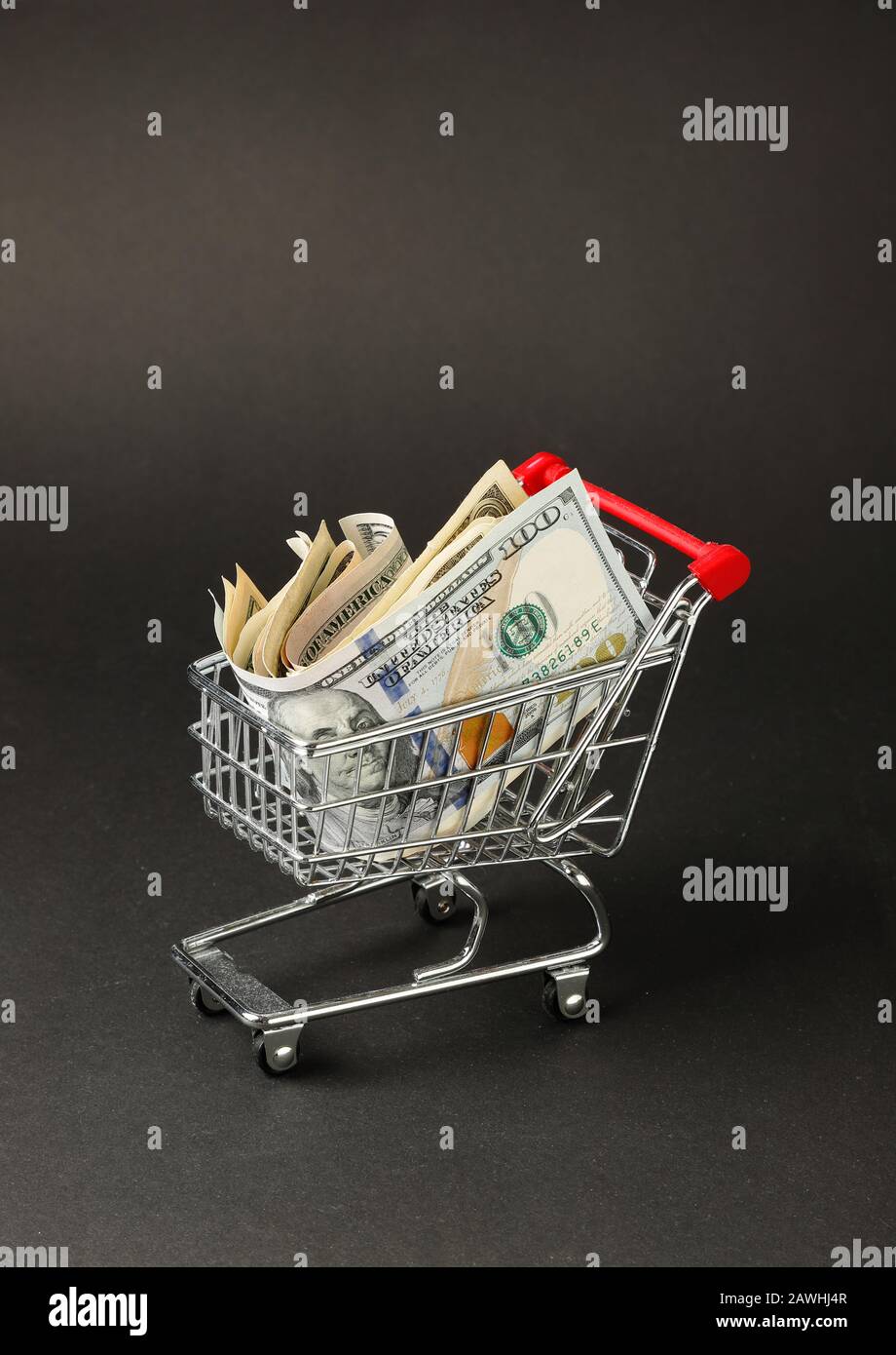 Un carrito de compras en miniatura lleno de billetes en dólares estadounidenses con fondo oscuro. Foto de stock
