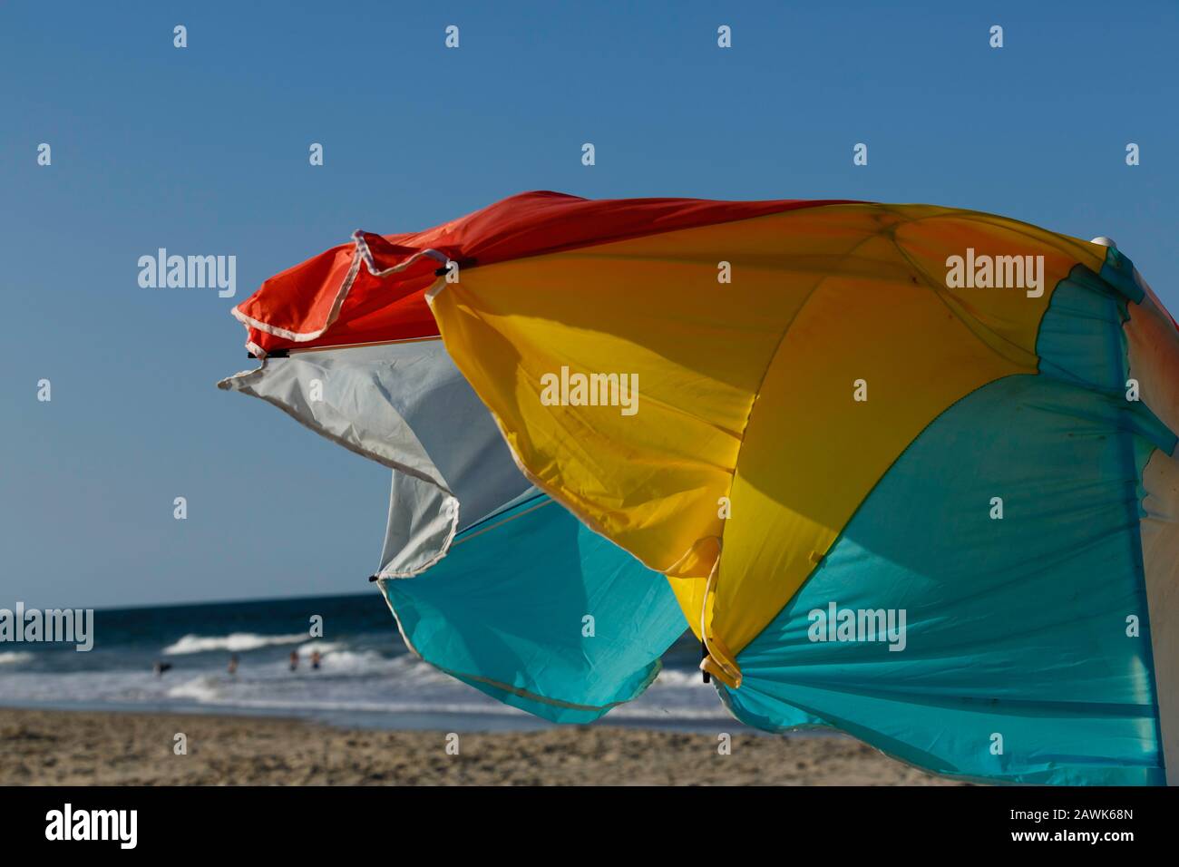Una sombrilla de colores brillantes y azotada por el viento que se colora en un día soleado perfecto en la playa Foto de stock