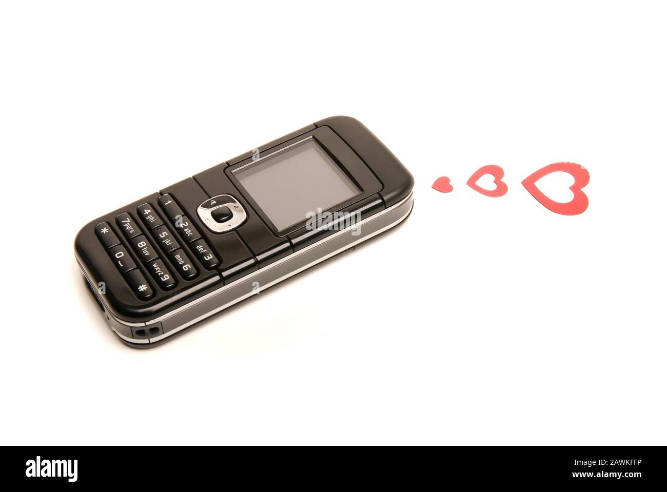 Teléfono móvil pasado de moda sobre fondo blanco con tres corazones rojos enviando un mensaje de amor Foto de stock