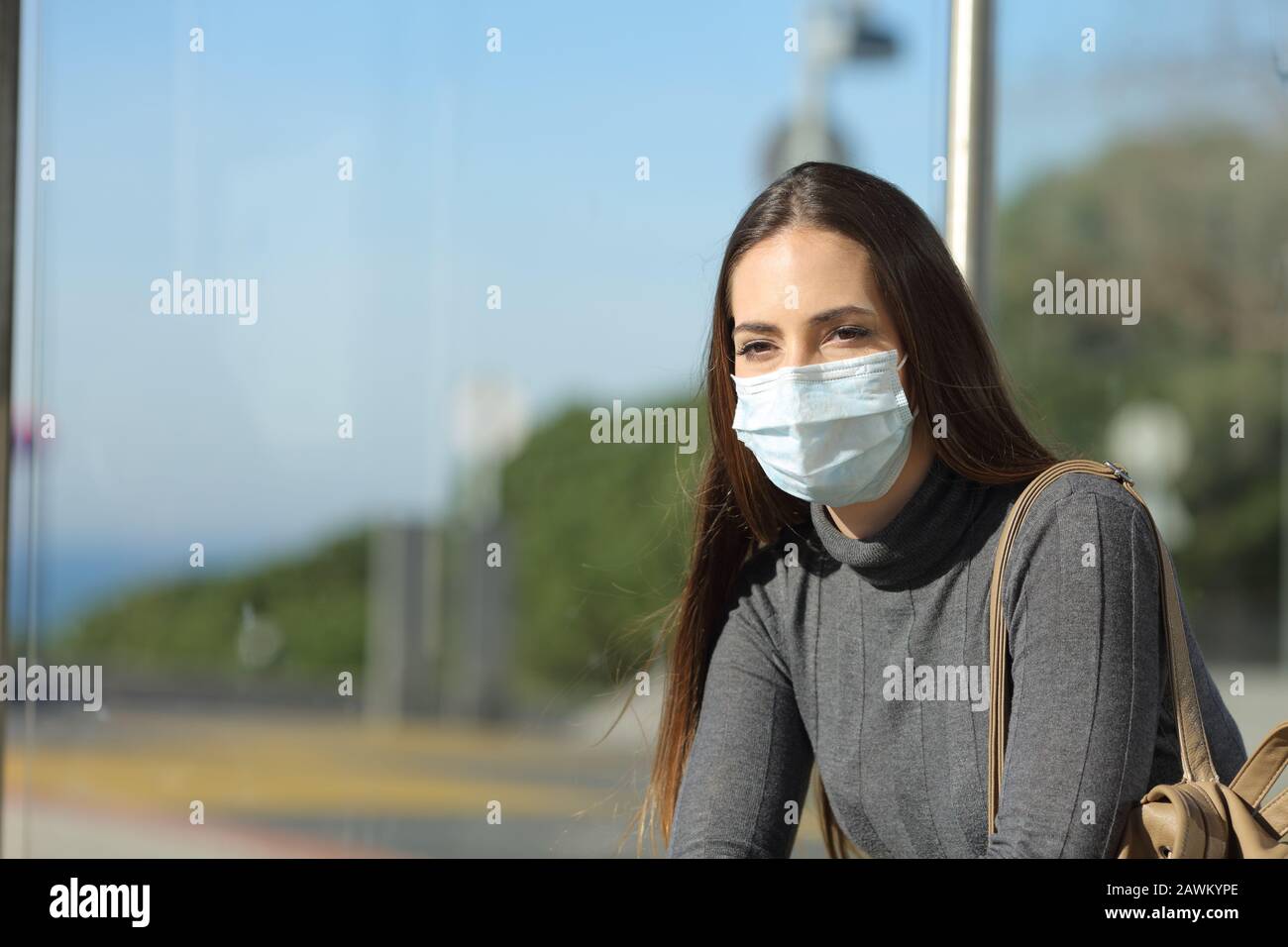 Mujer preocupada con una máscara que previene el contagio esperando en una parada de autobús Foto de stock