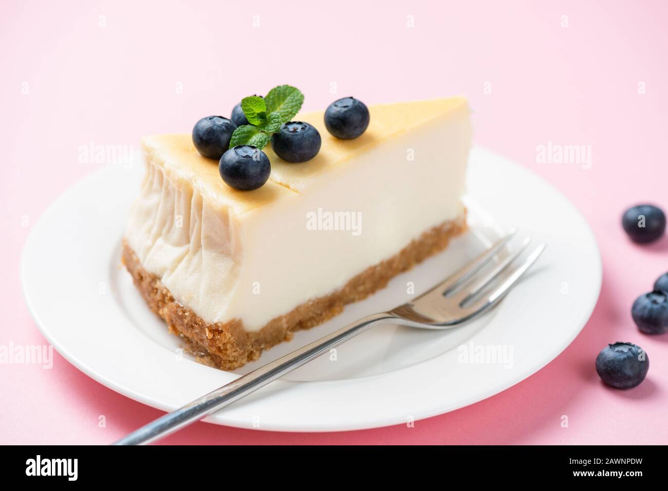 Rebanada de tarta de queso lisa con arándanos sobre fondo rosa Foto de stock
