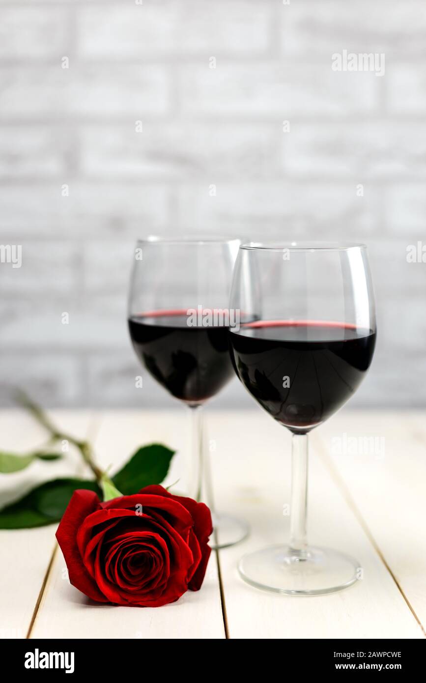 Concepto del día de San Valentín. Dos copas de vino y rosa roja sobre una mesa de madera blanca. Enfoque selectivo. Foto de stock