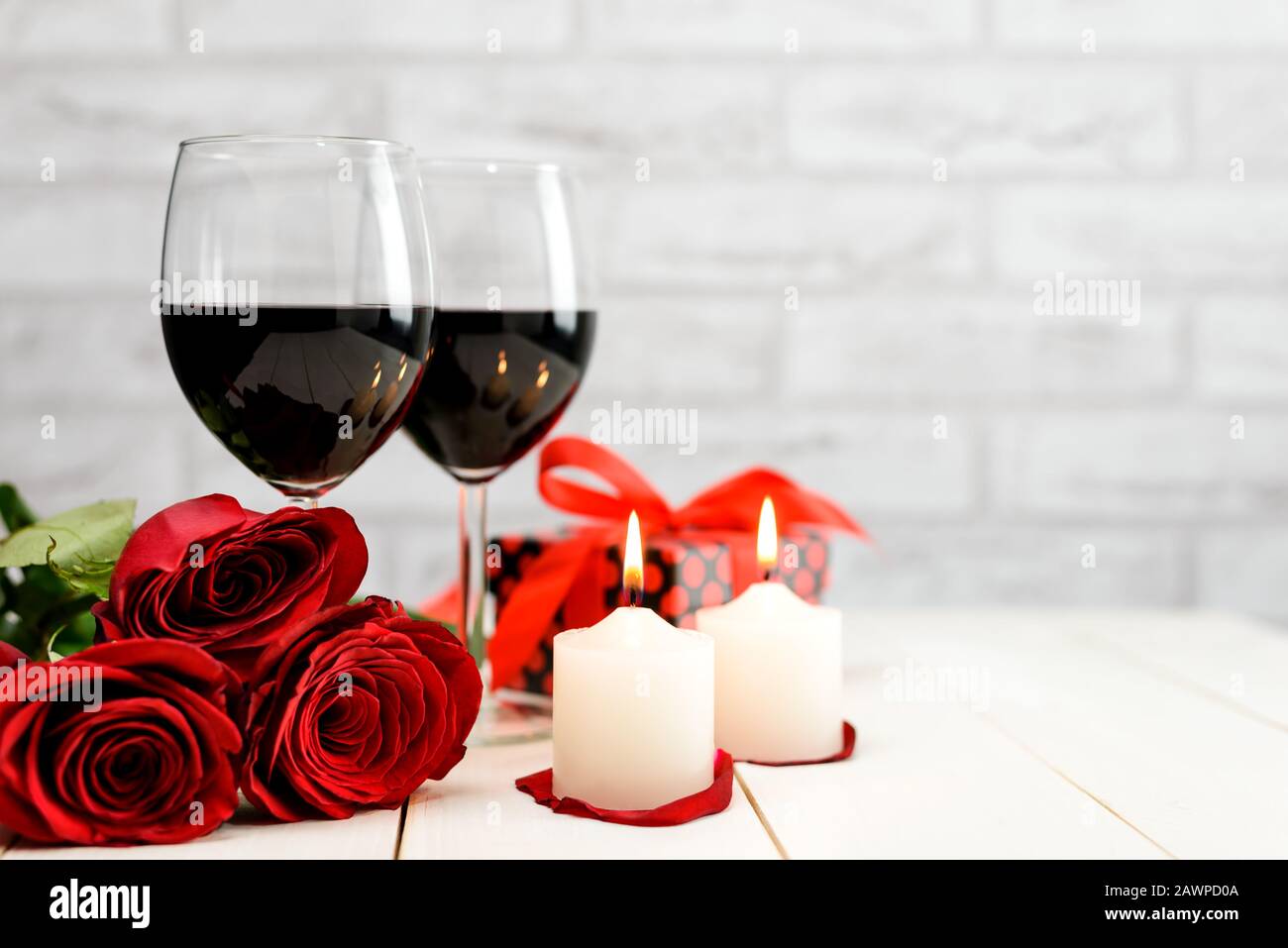 Concepto del día de San Valentín. Dos copas de vino, rosas rojas, caja de regalo y velas encendidas en una mesa de madera blanca con espacio para texto. Focu selectivo Foto de stock