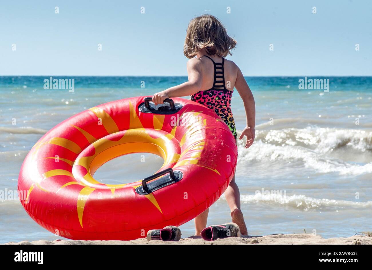 Una niña arranca sus zapatillas de deporte y se prepara para llevar su juguete flotante a las aguas activas del lago Michigan en los Estados Unidos Foto de stock