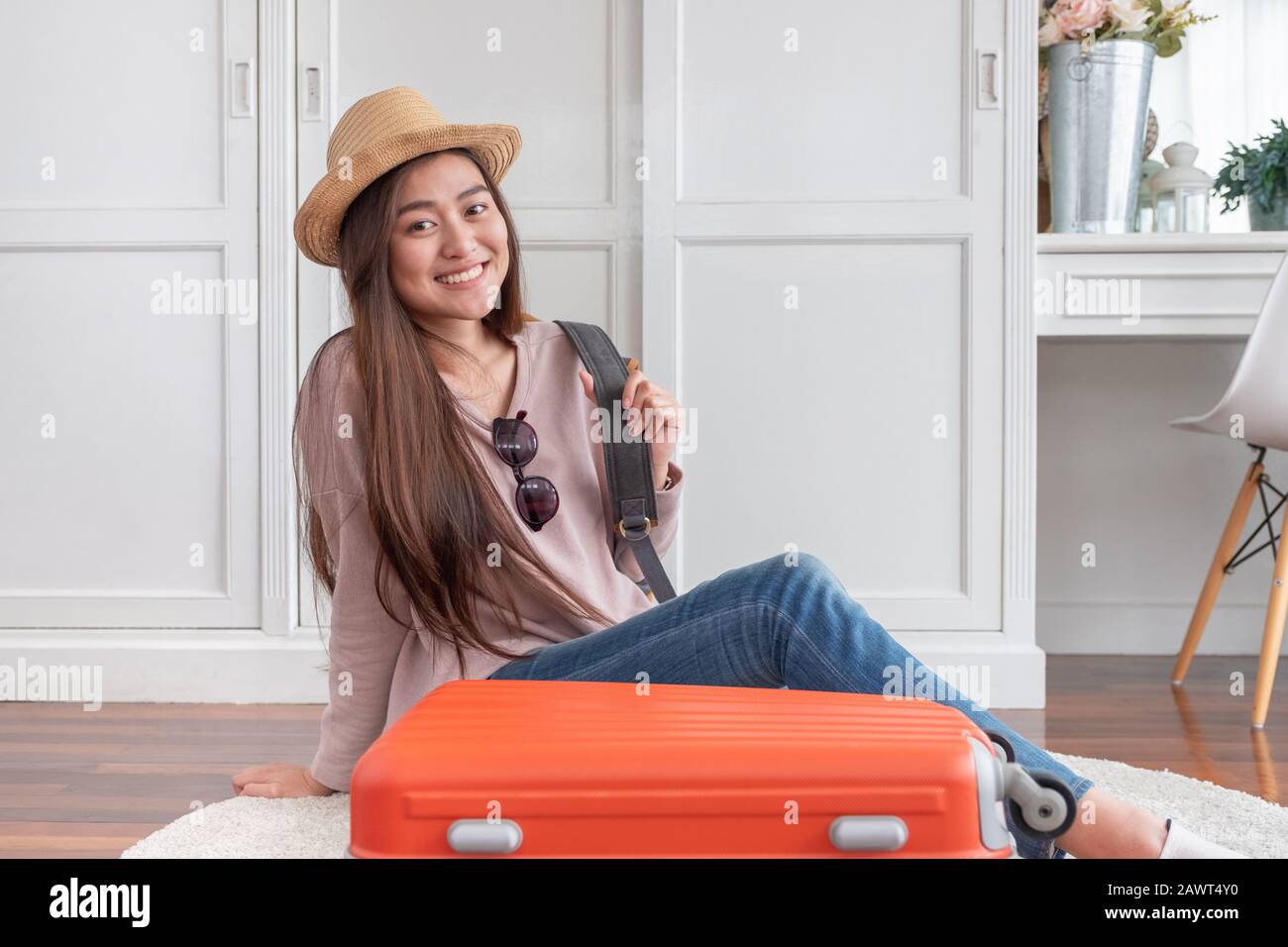 Una joven mujer asiática que viaja prepara ropa y cosas en una maleta naranja para unas vacaciones en casa. Concepto de viaje para mochileros Foto de stock