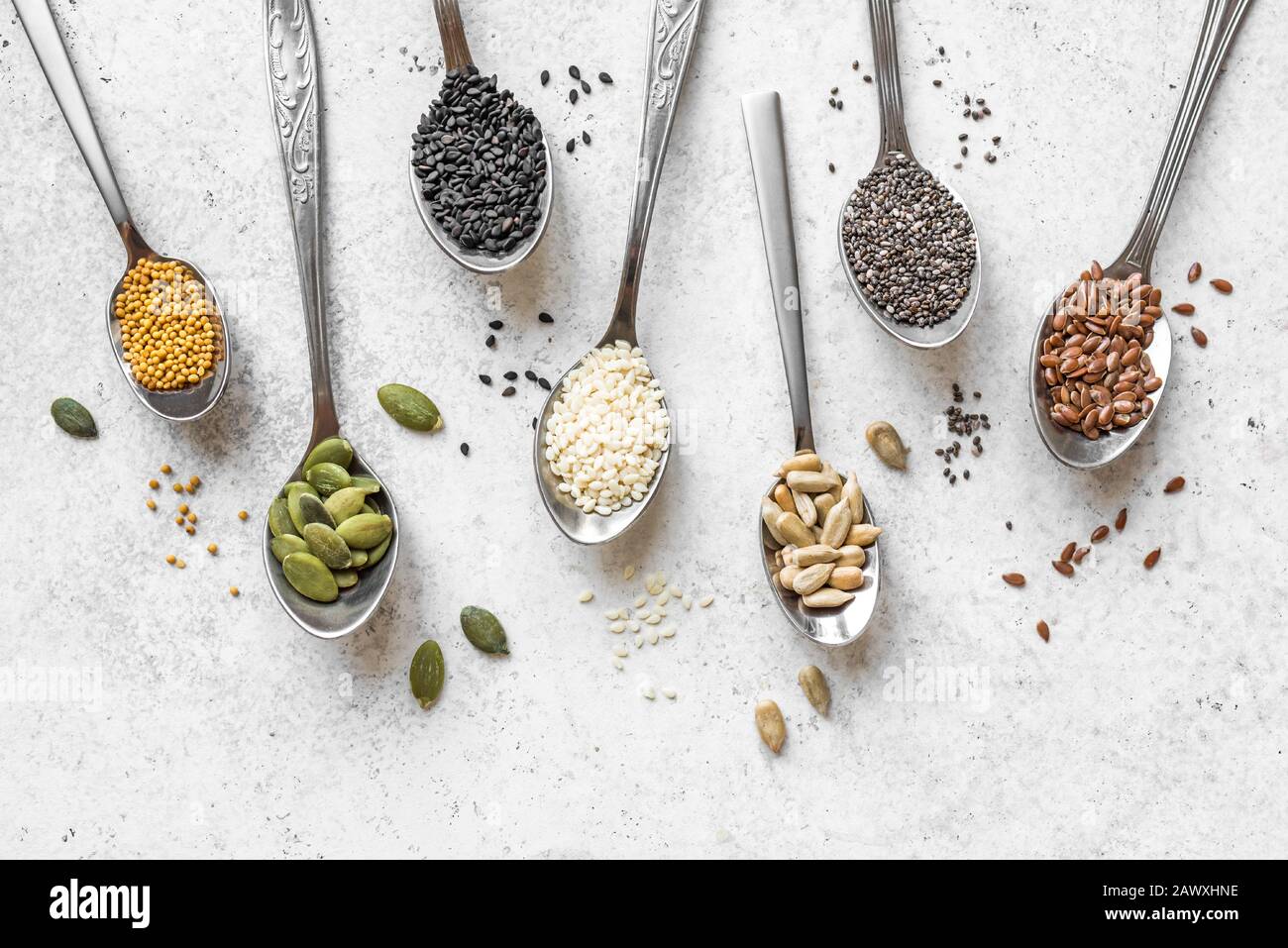 Surtido de varias semillas sobre fondo blanco. Conjunto de semillas de sésamo, semillas de lino, semillas de girasol, semillas de calabaza, chía, semillas de cáñamo en cucharas, alimentos saludables Foto de stock