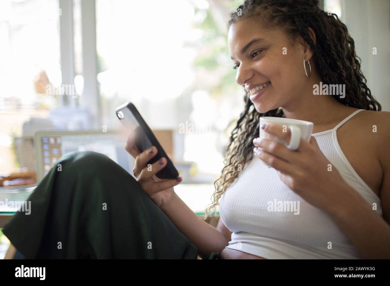 Mujer joven bebiendo café y usando un teléfono inteligente Foto de stock