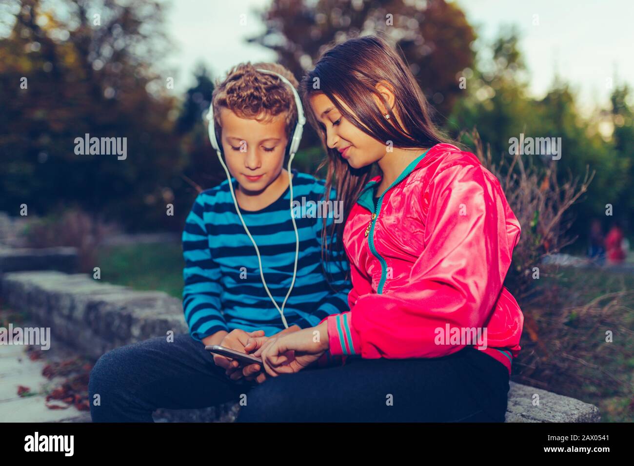 Felices pequeños amigos, chico y chica con auriculares que comparten