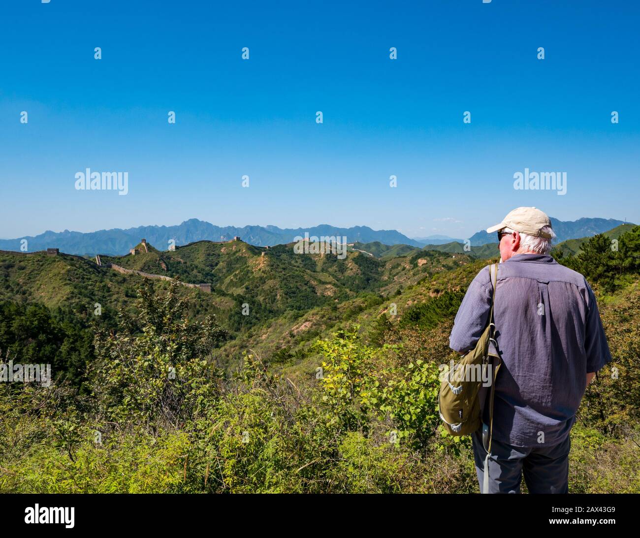 Senior European Male Tourist admirando la vista de la Gran Muralla Jinshanling de China en la cima de la montaña en clima soleado, China, Asia Foto de stock