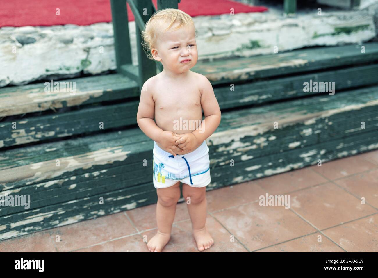 Lindo divertido disgustar caucásico niño de 2 años de edad de pie abandonado solo en la playa de día. Un niño asustado ofendido a sus padres durante las vacaciones Fotografía