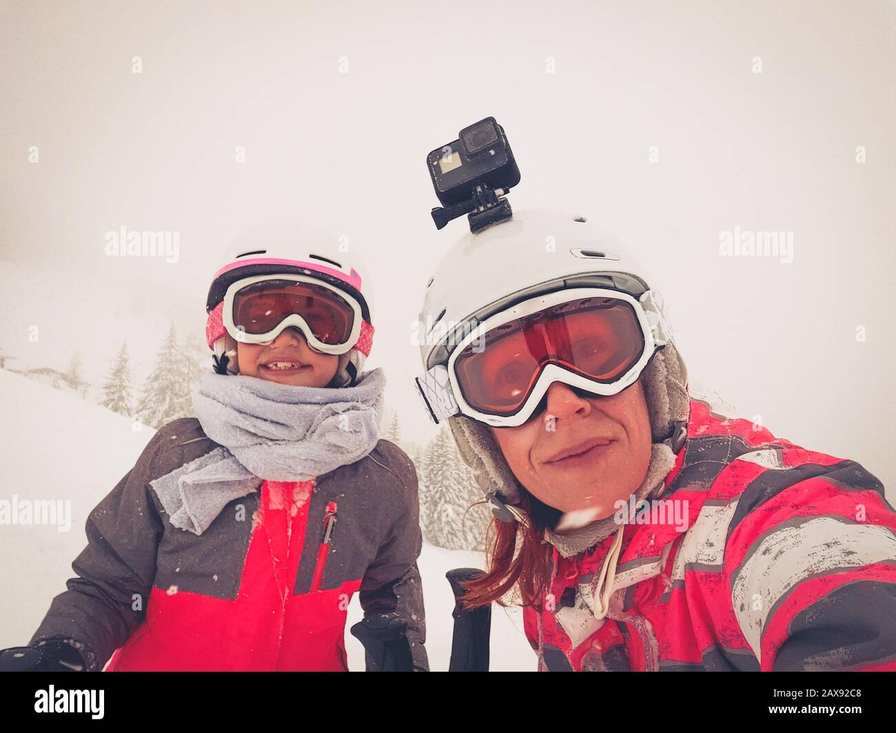 Familia en vacaciones de invierno tomando selfie en la ladera de la montaña. Familia y niños en equipo de esquí, cascos, gafas de esquí en la tormenta de huracanes ventiscas de nieve. Foto de stock