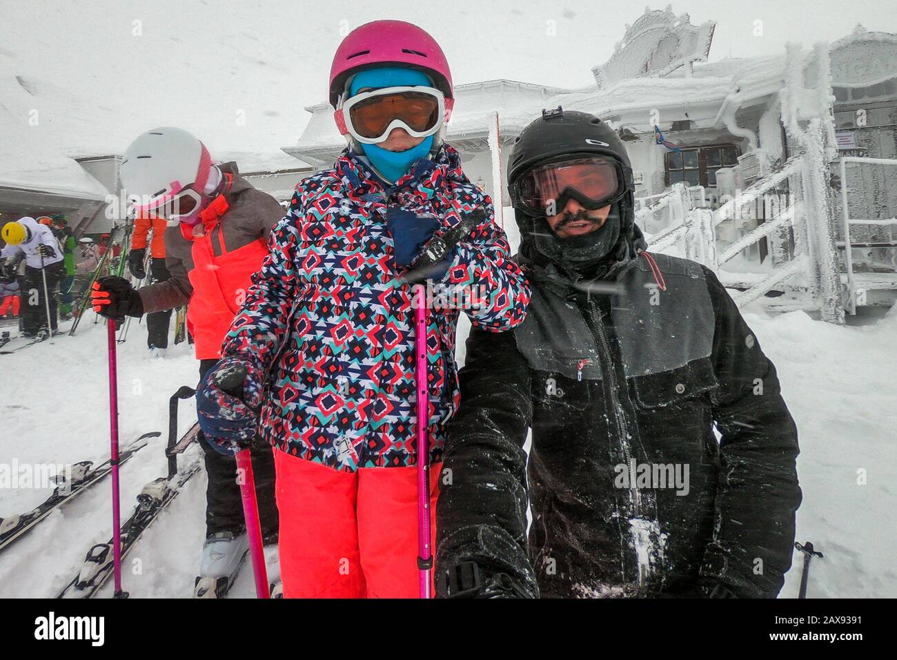 Familia en vacaciones de invierno tomando selfie en la ladera de la montaña. Familia y niños en equipo de esquí, cascos, gafas de esquí en la tormenta de huracanes ventiscas de nieve. Foto de stock