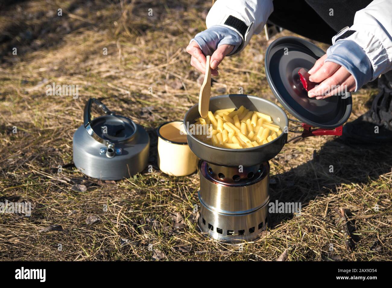 cerca de las manos de excursionista cocinar pasta en estufa de madera portátil. Cocinar pasta en las montañas Foto de stock