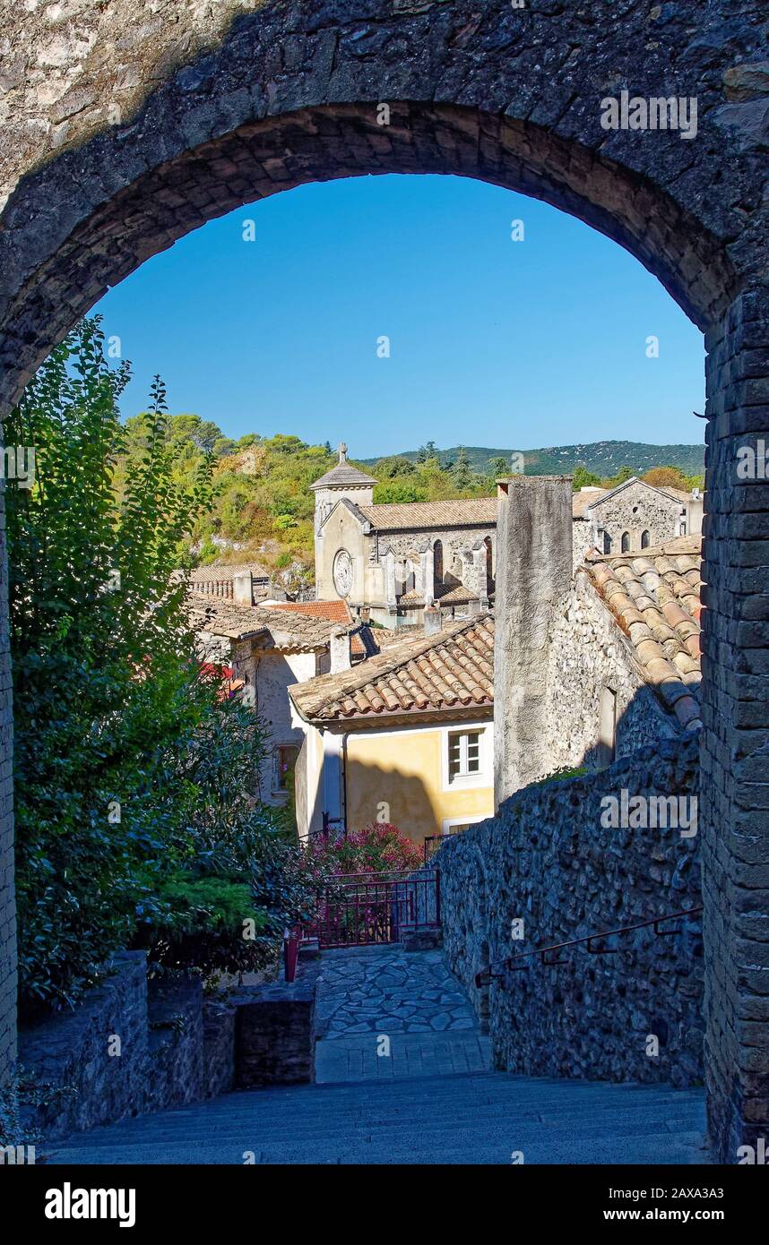 Vista de la ciudad a través del arco de piedra, edificios antiguos, tejados de tejas, Iglesia, empinados escalones, colinas, Viviers, Francia; verano, vertical Foto de stock