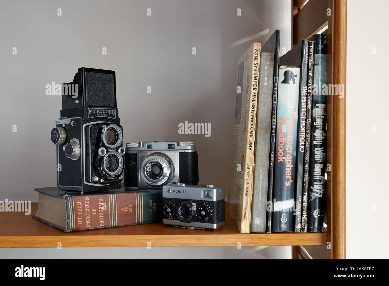 Una fotografía de tres cámaras y libros de fotografía vintage colocados en un estante. Foto de stock