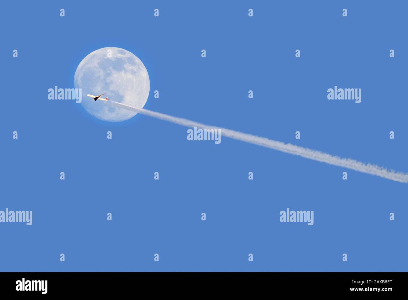Avión comercial de pasajeros / avión de pasajeros volando frente a la luna llena al anochecer mostrando contraindicaciones / senderos de condensación Foto de stock