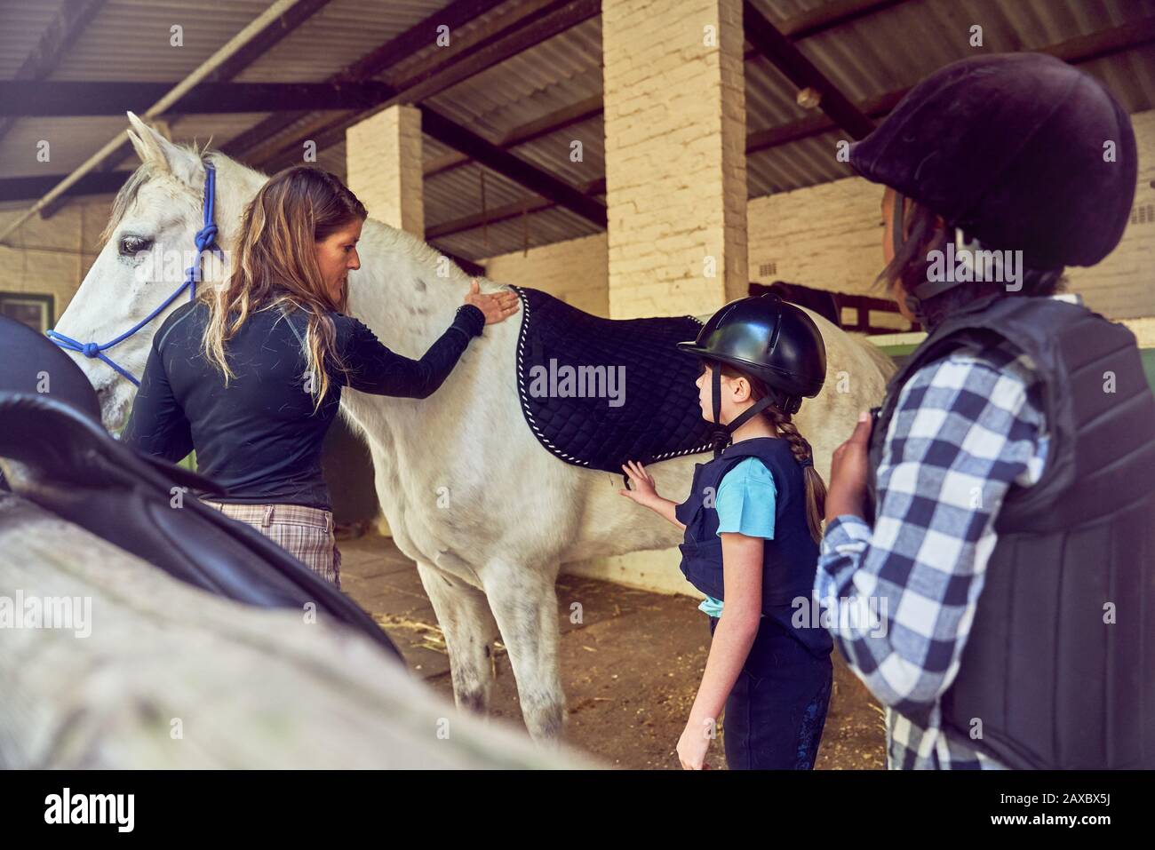 Instructor femenino ayudando a las niñas a prepararse para montar a caballo Foto de stock
