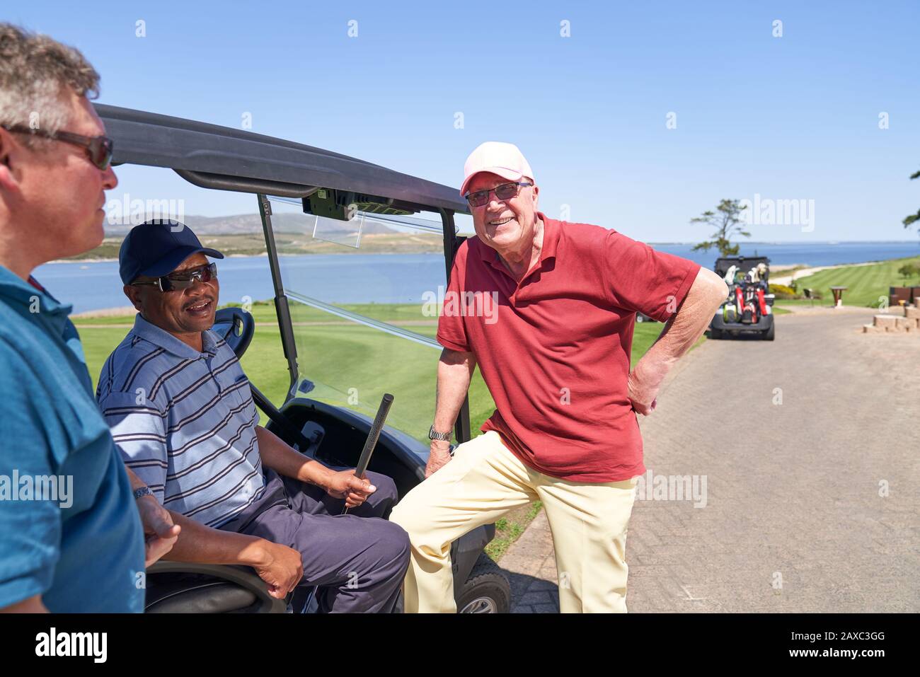 Feliz hombre golfista amigos hablando en carrito de golf en el campo soleado Foto de stock