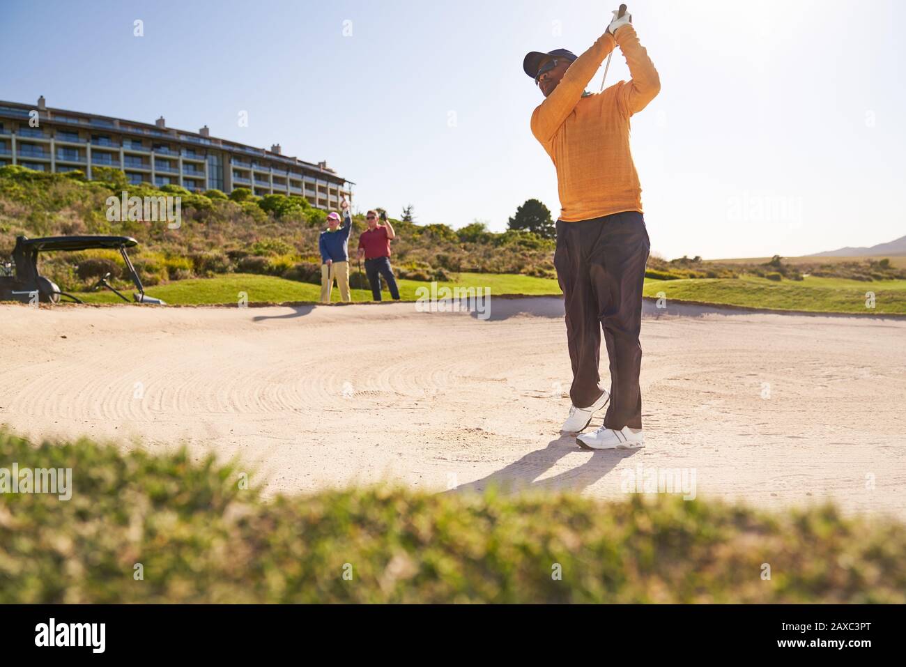 Golfista masculino tomando un tiro de búnker soleado Foto de stock