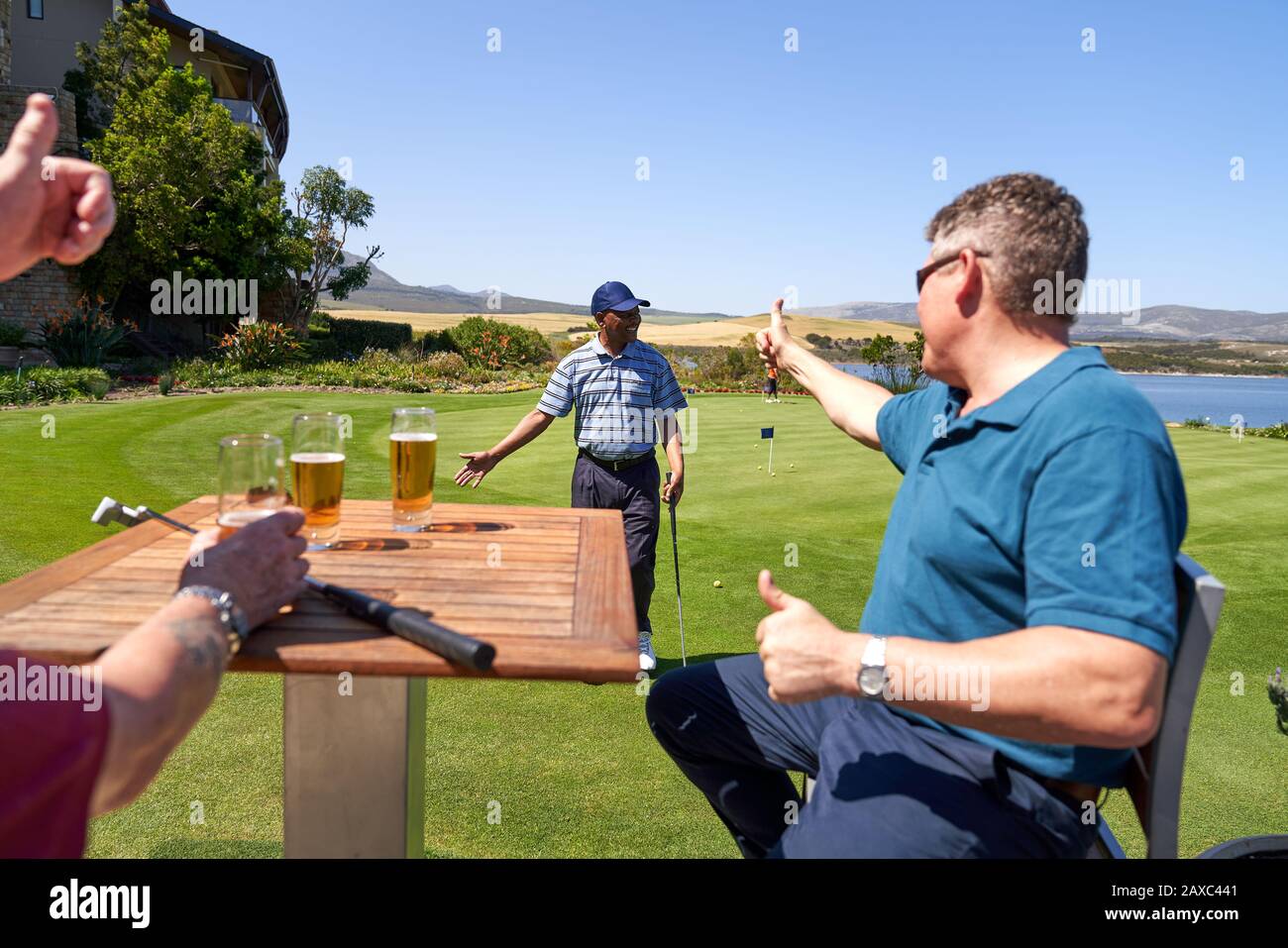 Los golfistas masculinos bebiendo cerveza animando a amigo en la práctica poniendo verde Foto de stock