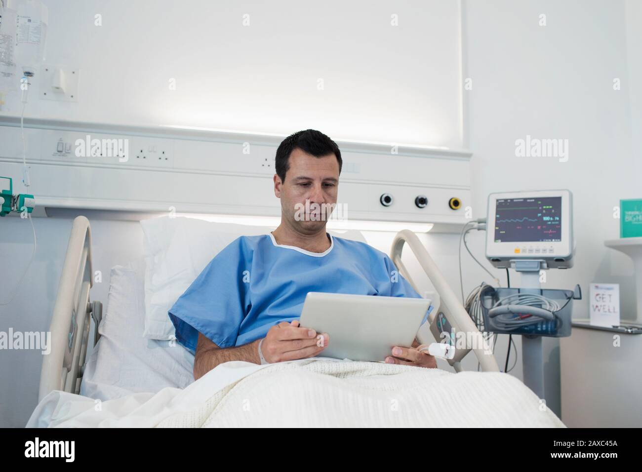 Paciente masculino con tableta digital, descansando en la cama del hospital Foto de stock