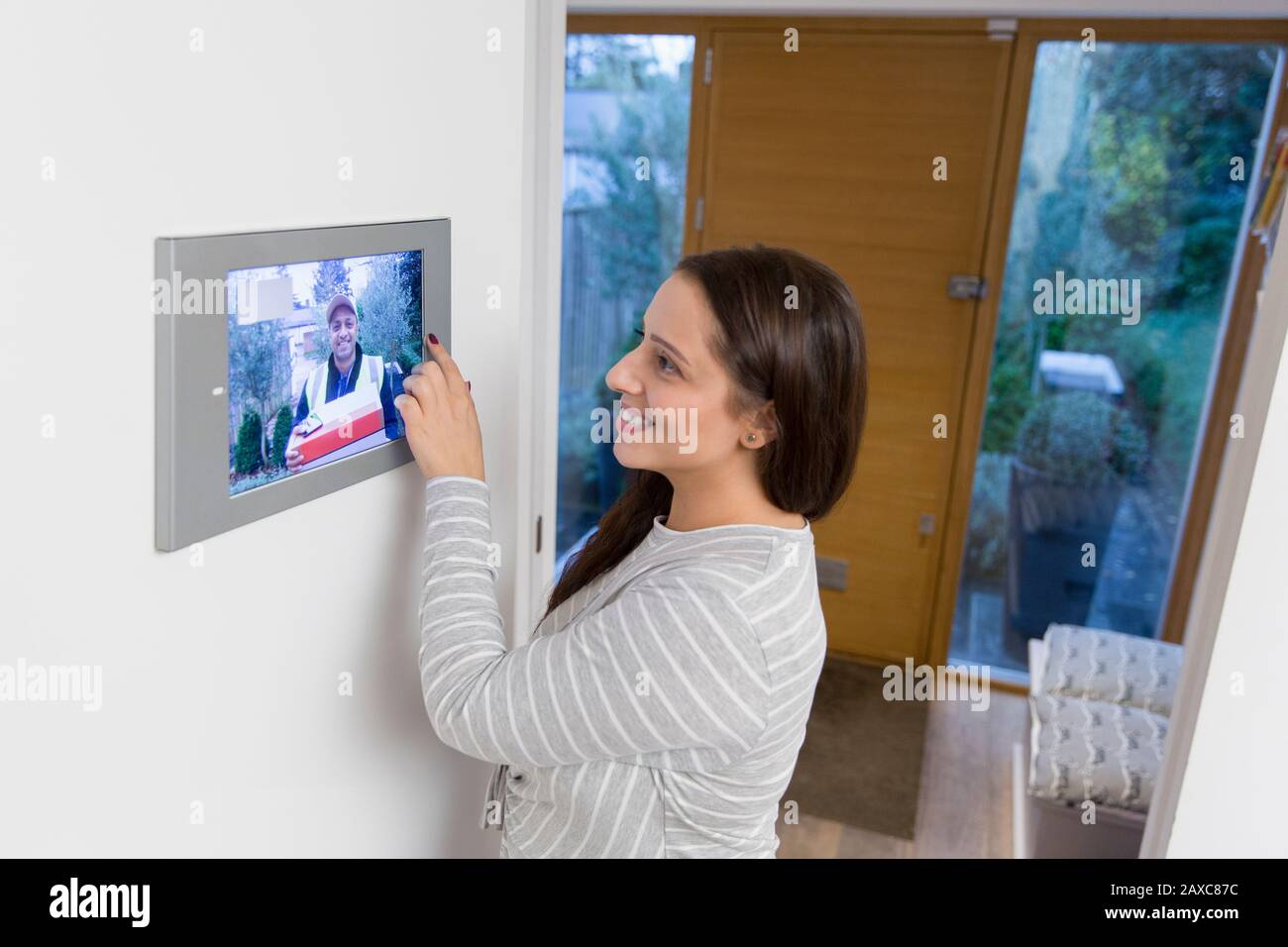 Mujer sonriente viendo a deliveryman acercándose a la puerta principal desde la pantalla inteligente de automatización de casa Foto de stock