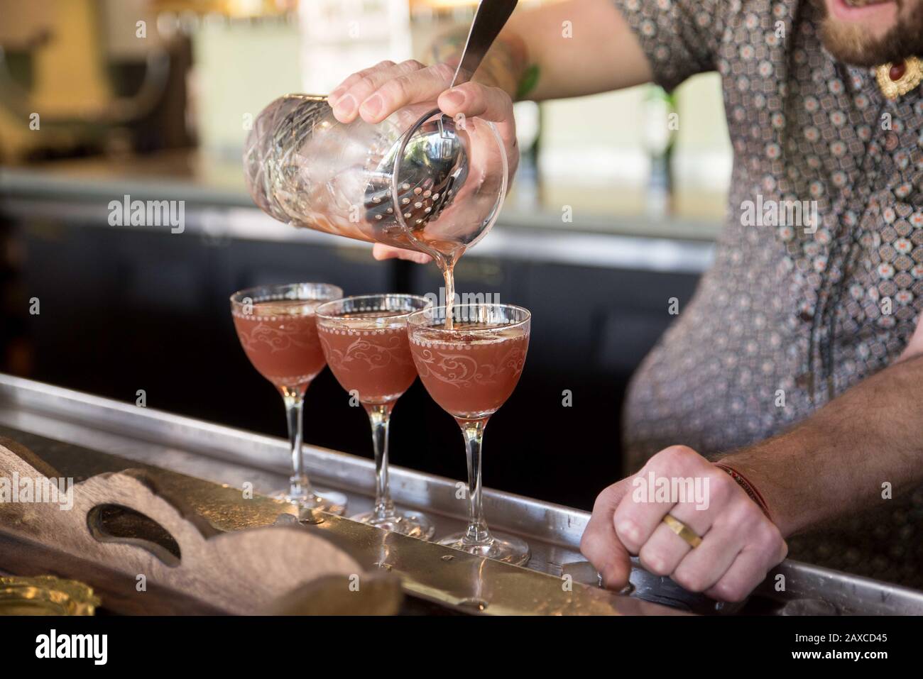 Un barman que vierte 3 cócteles de un agitador en la cristalería Nick & Nora. Foto de stock