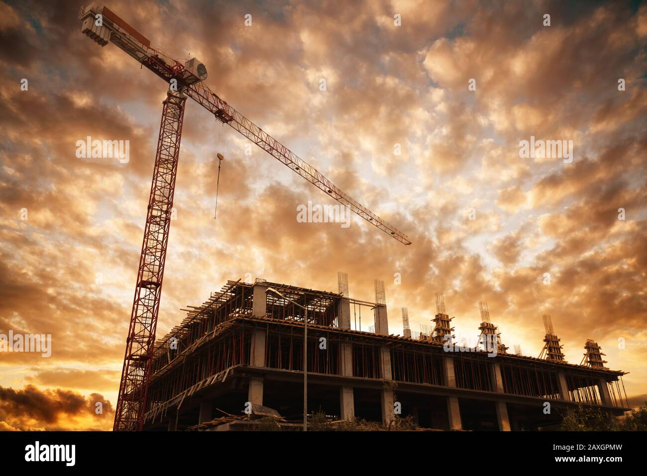 Silueta de un edificio con una grúa de construcción contra la puesta de sol y las nubes. Edificios y concepto de construcción Foto de stock