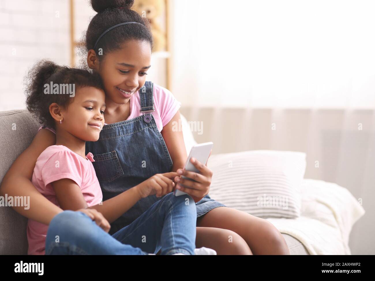 Niña afroamericana jugando en el celular de su hermana Foto de stock
