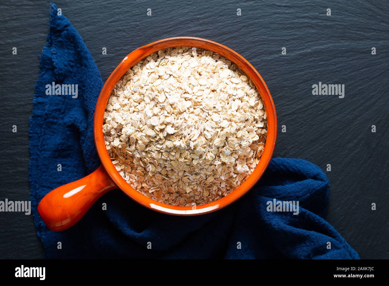 Concepto de comida saludable avena Orgánica Enrollada de grano entero en un tazón de naranja con servilletas azules sobre fondo negro de piedra de pizarra Foto de stock