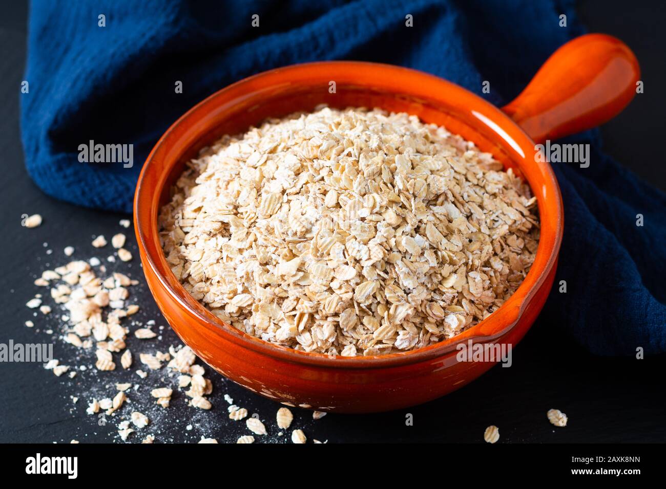 Concepto de comida saludable avena Orgánica Enrollada de grano entero en un tazón de naranja con servilletas azules sobre fondo negro de piedra de pizarra Foto de stock