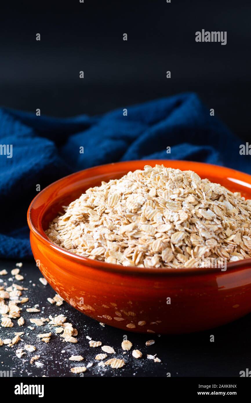 Concepto de comida saludable avena Orgánica Enrollada de grano entero en un tazón de naranja con servilletas azules sobre fondo negro de piedra de pizarra Foto de stock