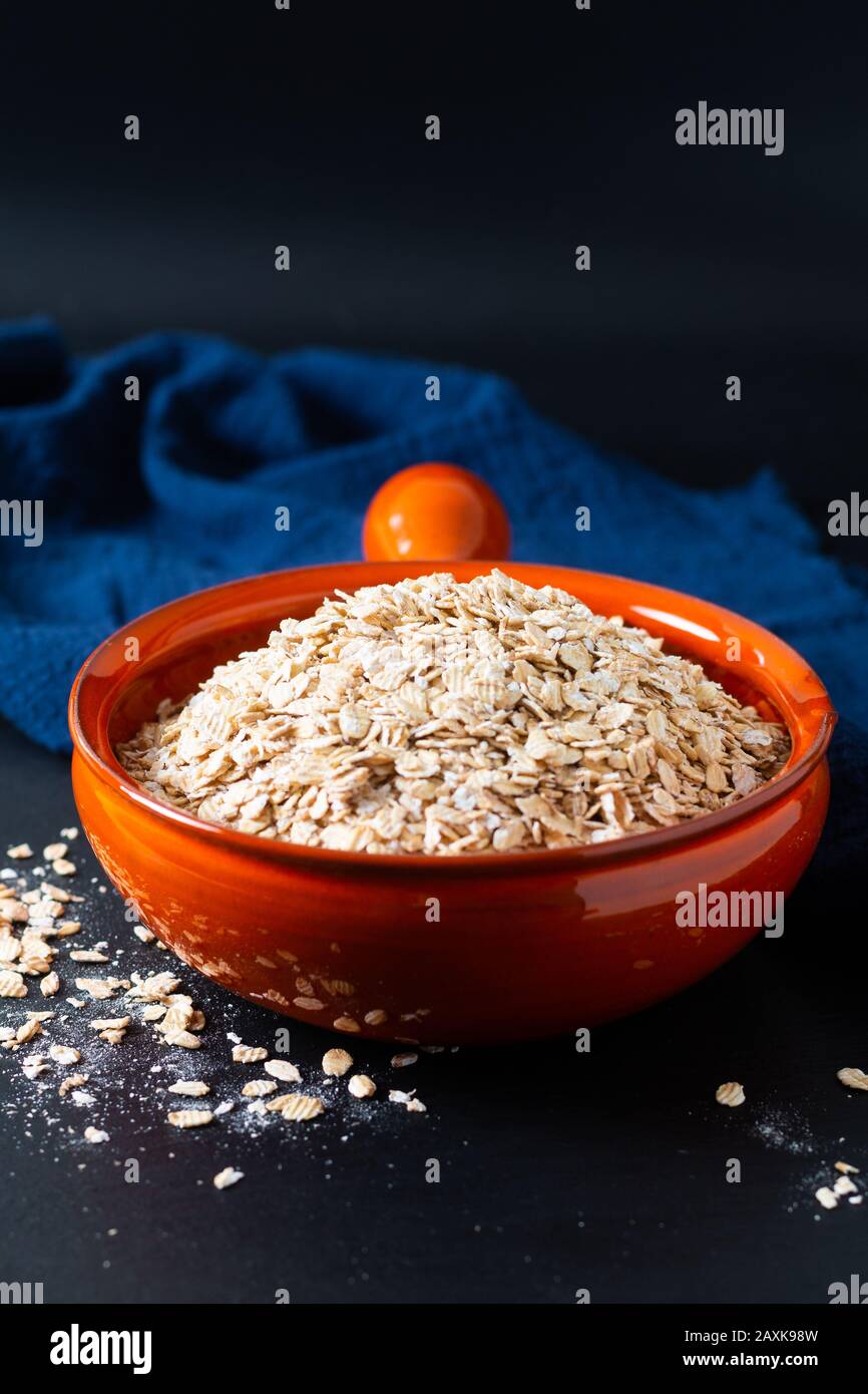 Concepto de comida saludable avena Orgánica Enrollada de grano entero en un tazón de naranja con servilletas azules sobre fondo negro de piedra de pizarra Foto de stock