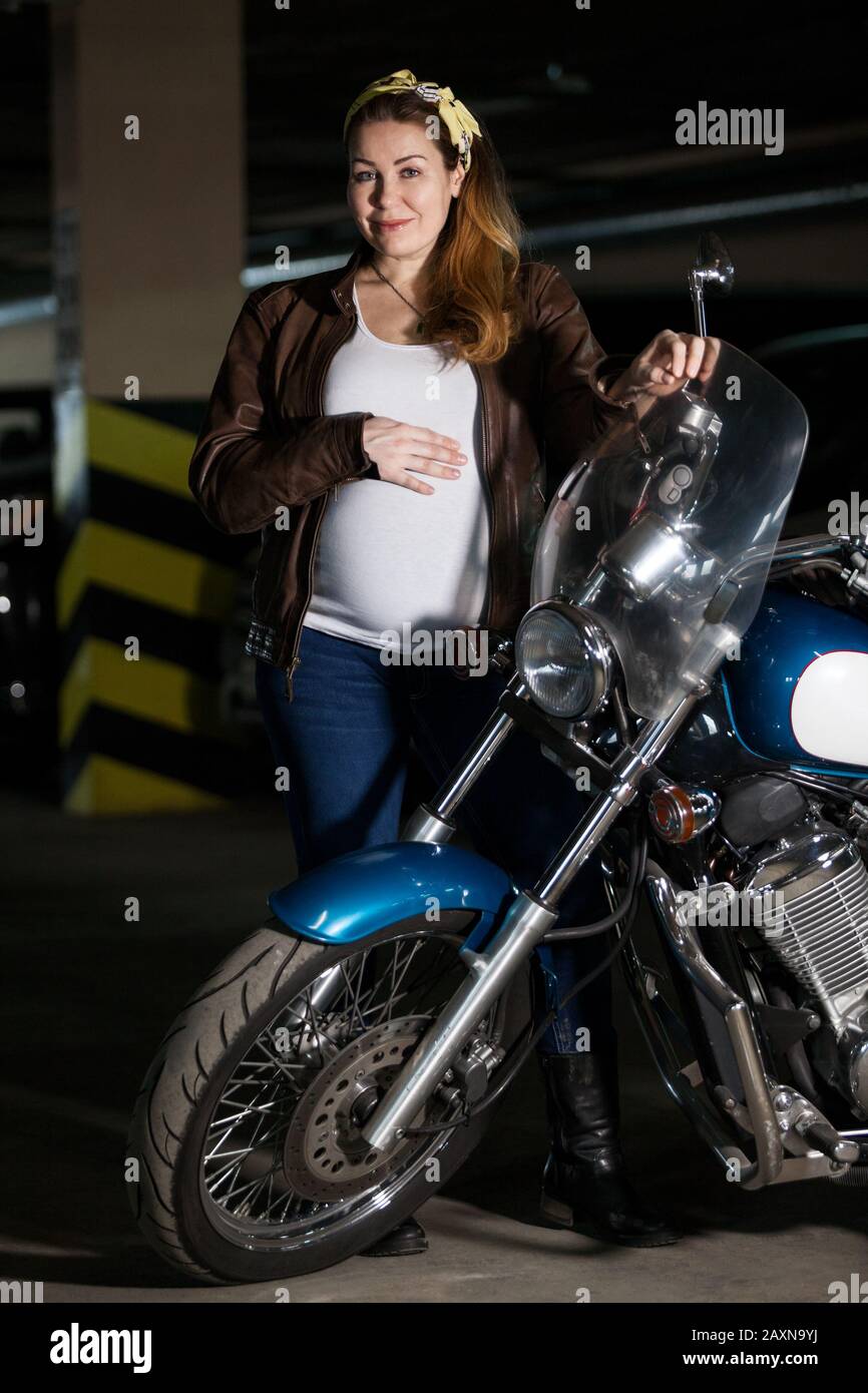 Mujer caucásica embarazada vestida con chaqueta de cuero marrón de pie con motocicleta, sosteniendo el volante y su gran vientre Fotografía de - Alamy