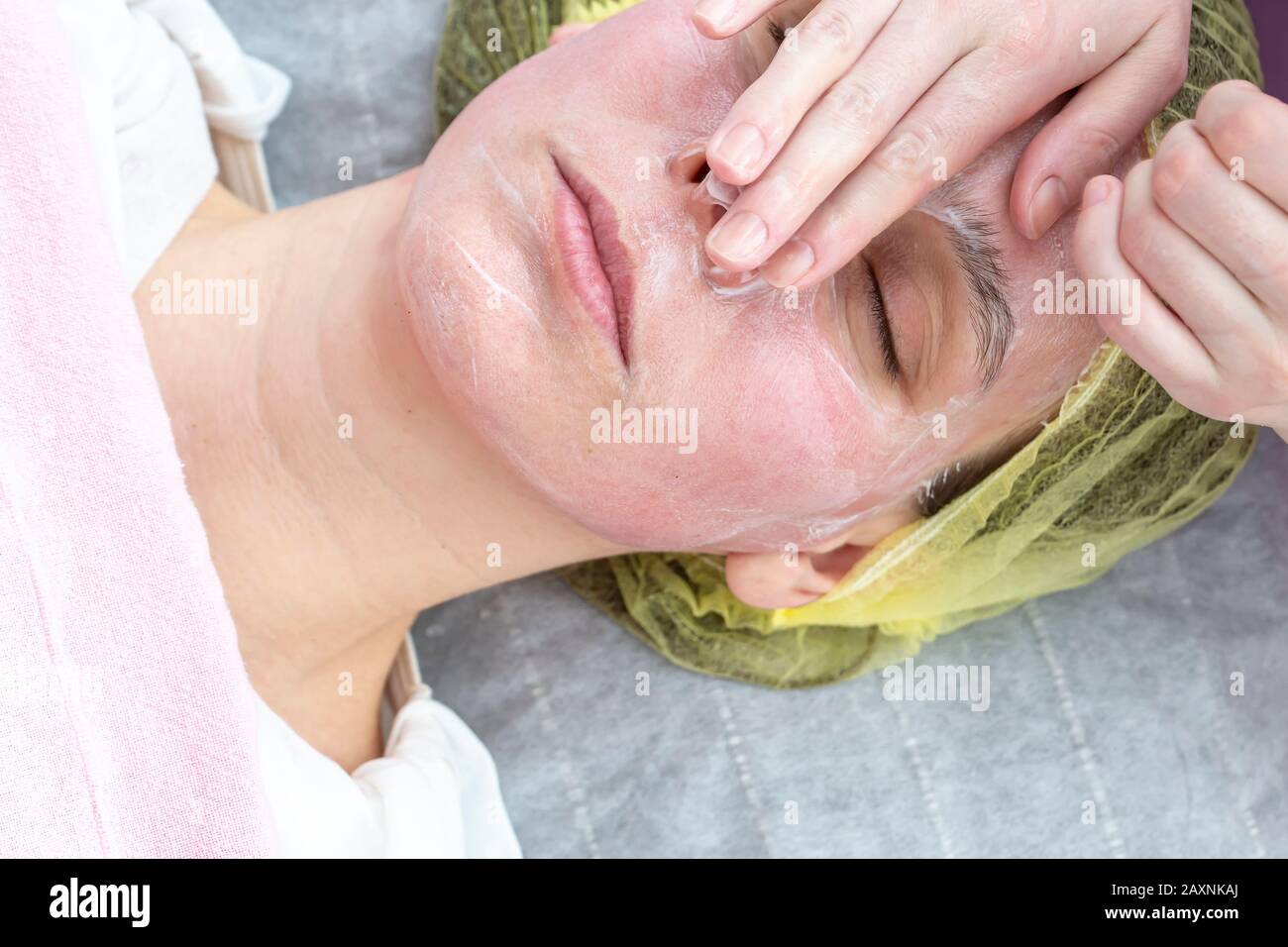 Limpieza facial profunda de la cara de una mujer con las manos y una  cuchara de un esteticista en guantes. En el salón con una toalla blanca.  Cosmetólogo usando Fotografía de stock 