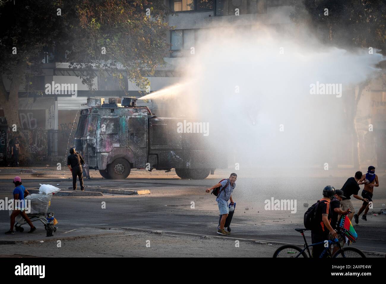 Camión blindado de policía con cañón de agua rociando agua sobre manifestantes durante manifestaciones recientes en la Plaza de Italia en Santiago de Chile. Foto de stock