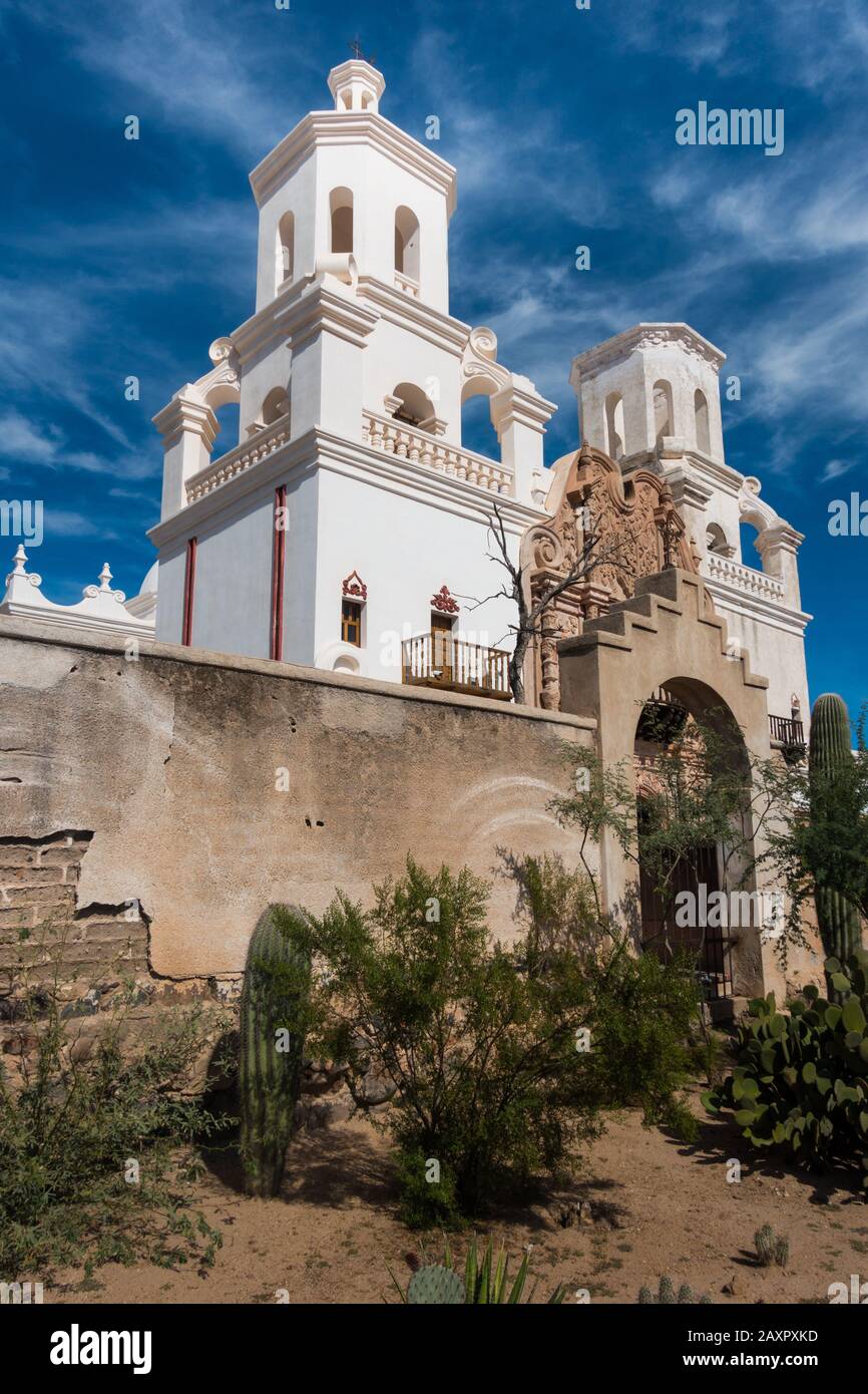 Hermosa Misión antigua en Tucson Arizona con torre de la iglesia y entrada histórica. Cactus creciendo frente a las paredes de la misión. Hermoso cielo azul con pocos Foto de stock