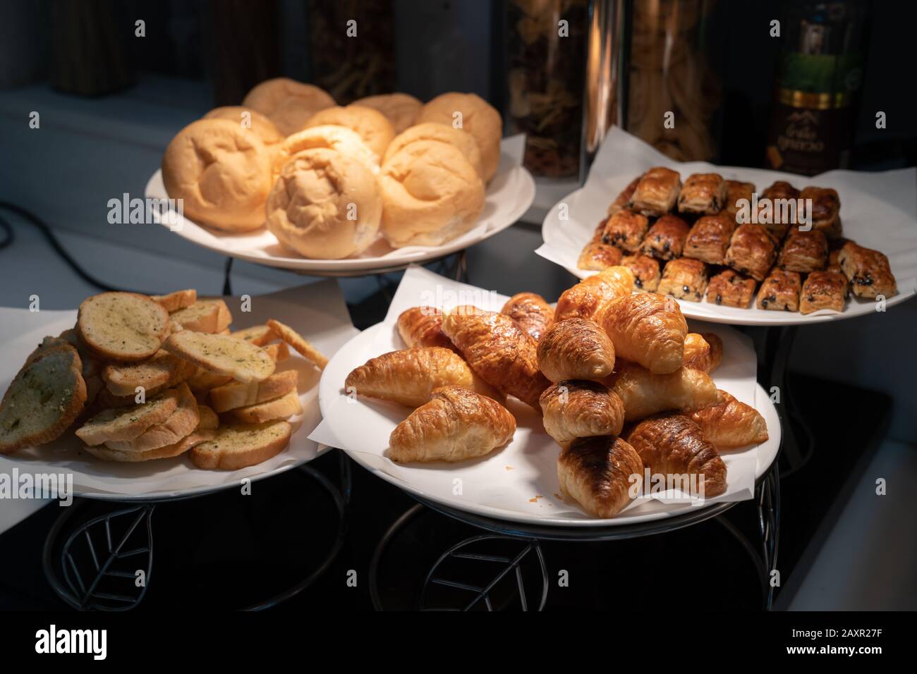 El croissant y el pan en papel y el plato blanco en la oscuridad están decorados con luz de tungsteno de la lámpara. Foto de stock