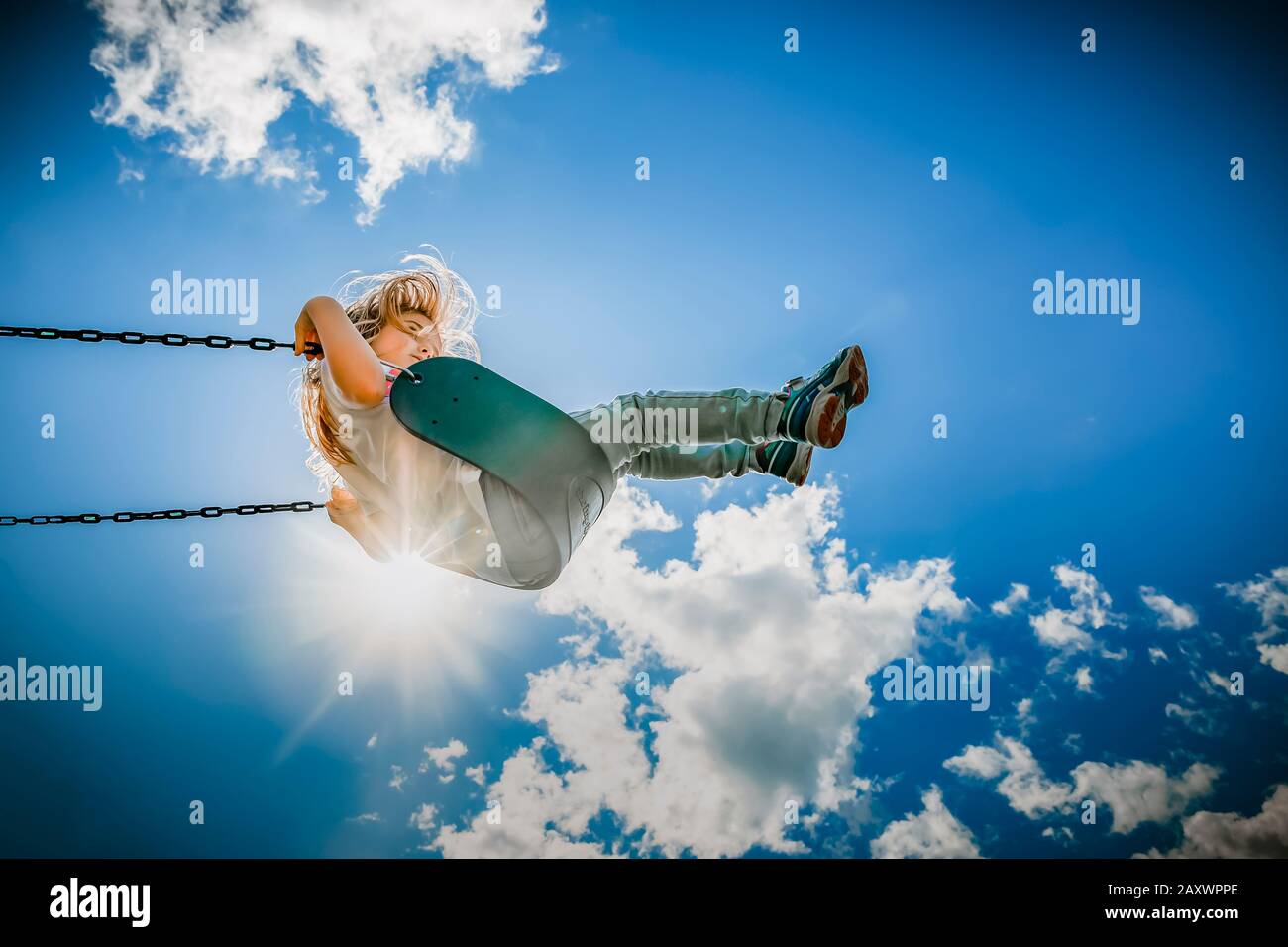 chica en un columpio alcanzando las nubes en una tarde de verano caliente Foto de stock