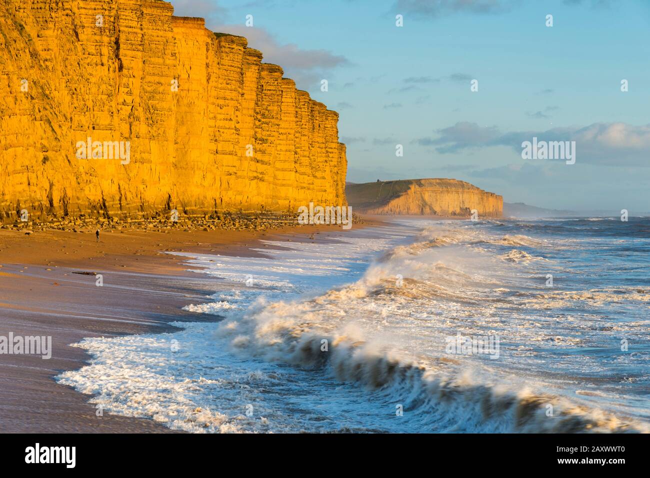 West Bay, Dorset, Reino Unido. 13 de febrero de 2020. Clima en el Reino Unido. Los mares accidentados rompen en tierra en East Beach, en West Bay, en Dorset, mientras los acantilados de arenisca brillan en una naranja dorada en una tarde soleada poco antes de la puesta de sol. Crédito De La Imagen: Graham Hunt/Alamy Live News Foto de stock