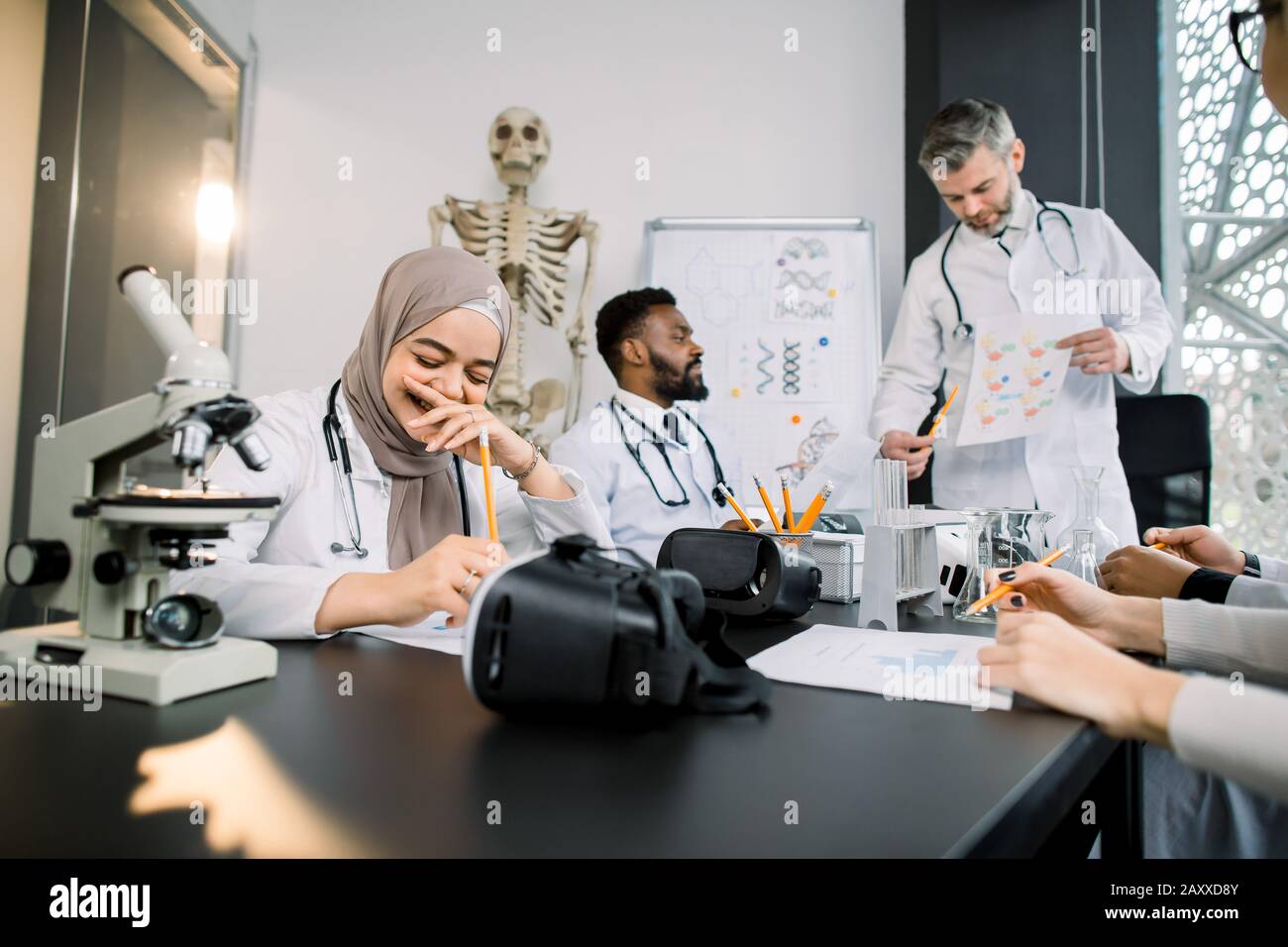 Hermoso profesor masculino con estudiantes de medicina multiétnica o científicos que usan batas de laboratorio en el salón de clase. Joven y bonita niña musulmana es feliz y sonriente Foto de stock