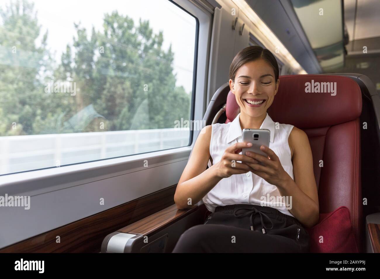 Sonriente mujer de negocios asiática con la aplicación de redes sociales para smartphones mientras se desplazaba al trabajo en tren. Mujer sentada en el transporte disfrutando del viaje. Foto de stock