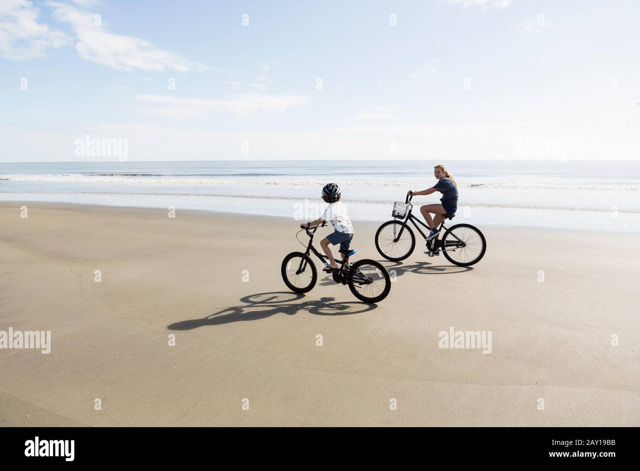 Hermanos, un niño y una niña que pedalan en bicicleta en una playa. Foto de stock