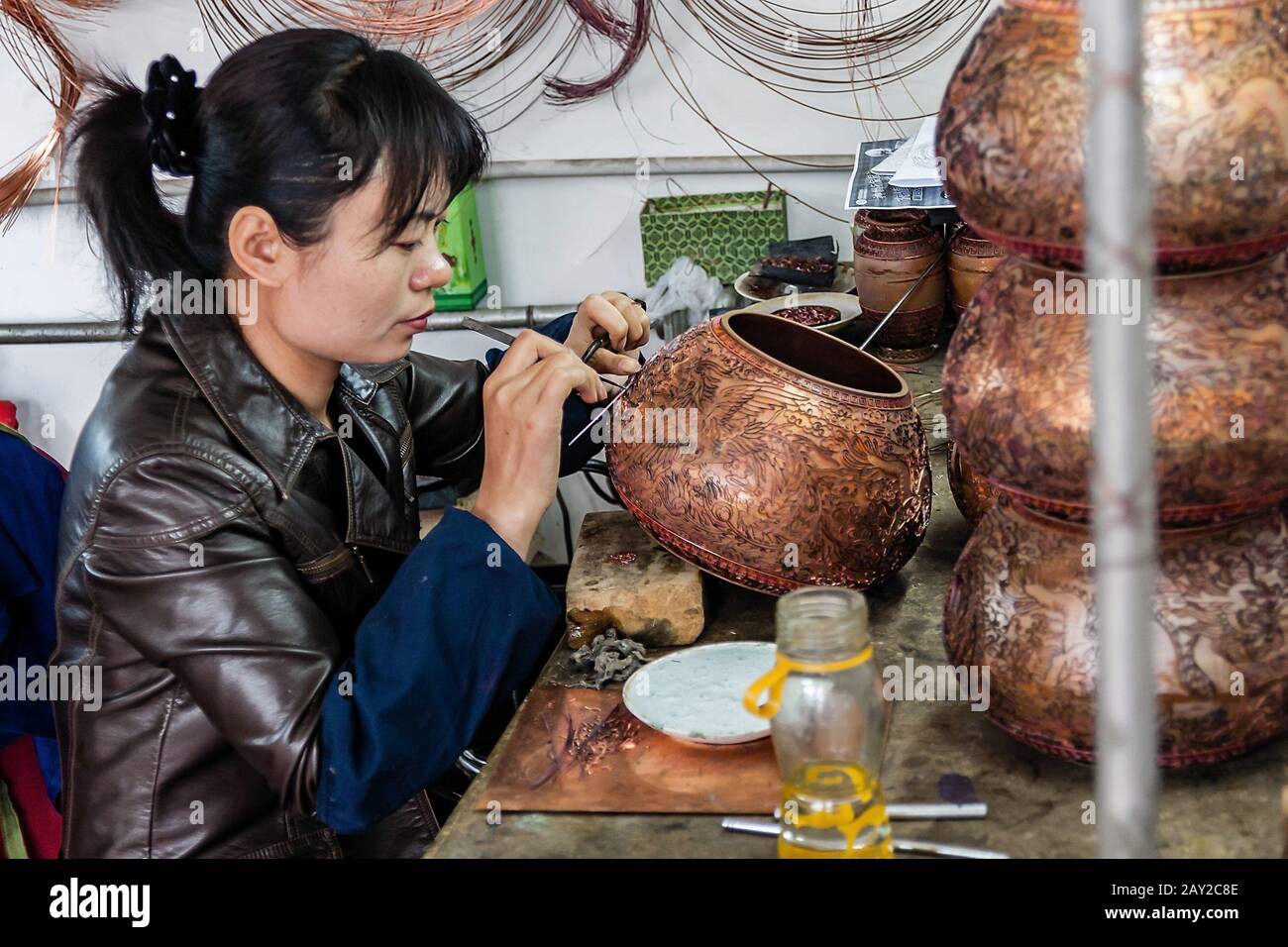 Una joven trabajadora China que graba un jarrón de cobre Foto de stock