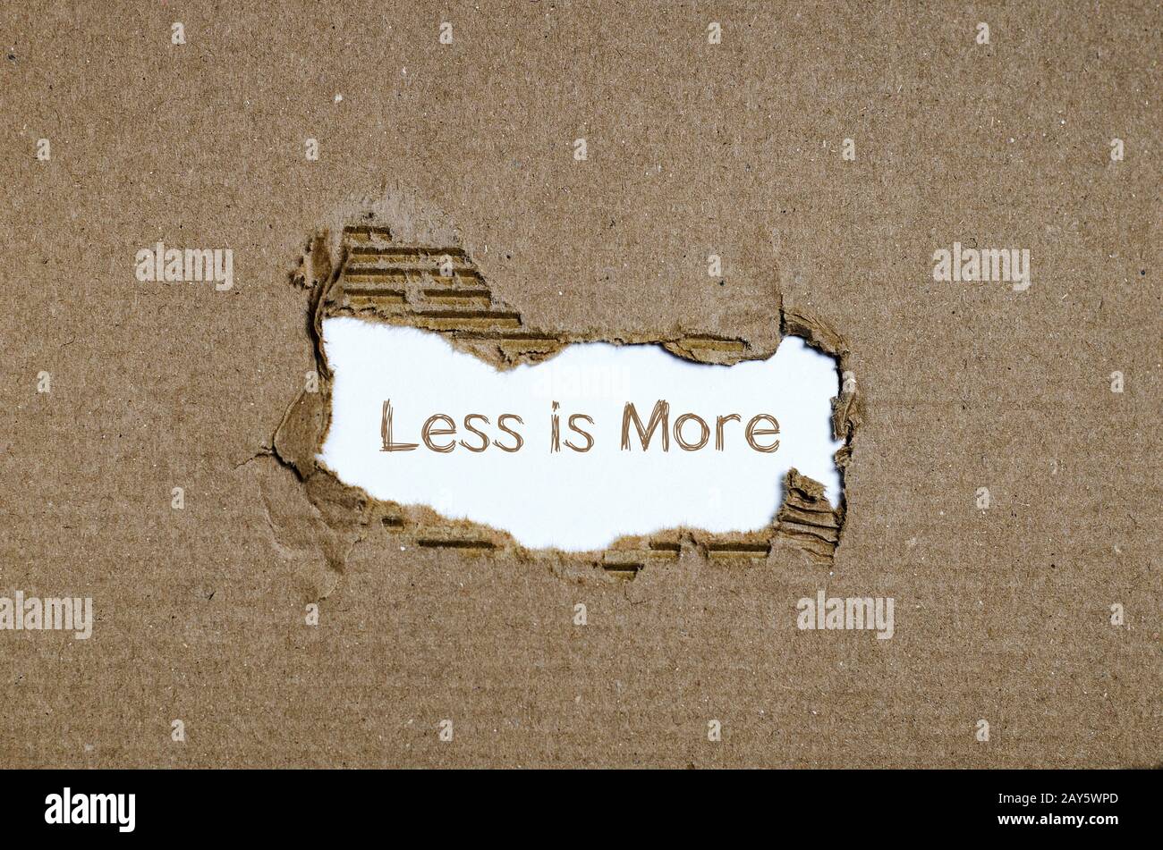 La palabra menos es más que aparecen detrás de papel rasgado. Foto de stock