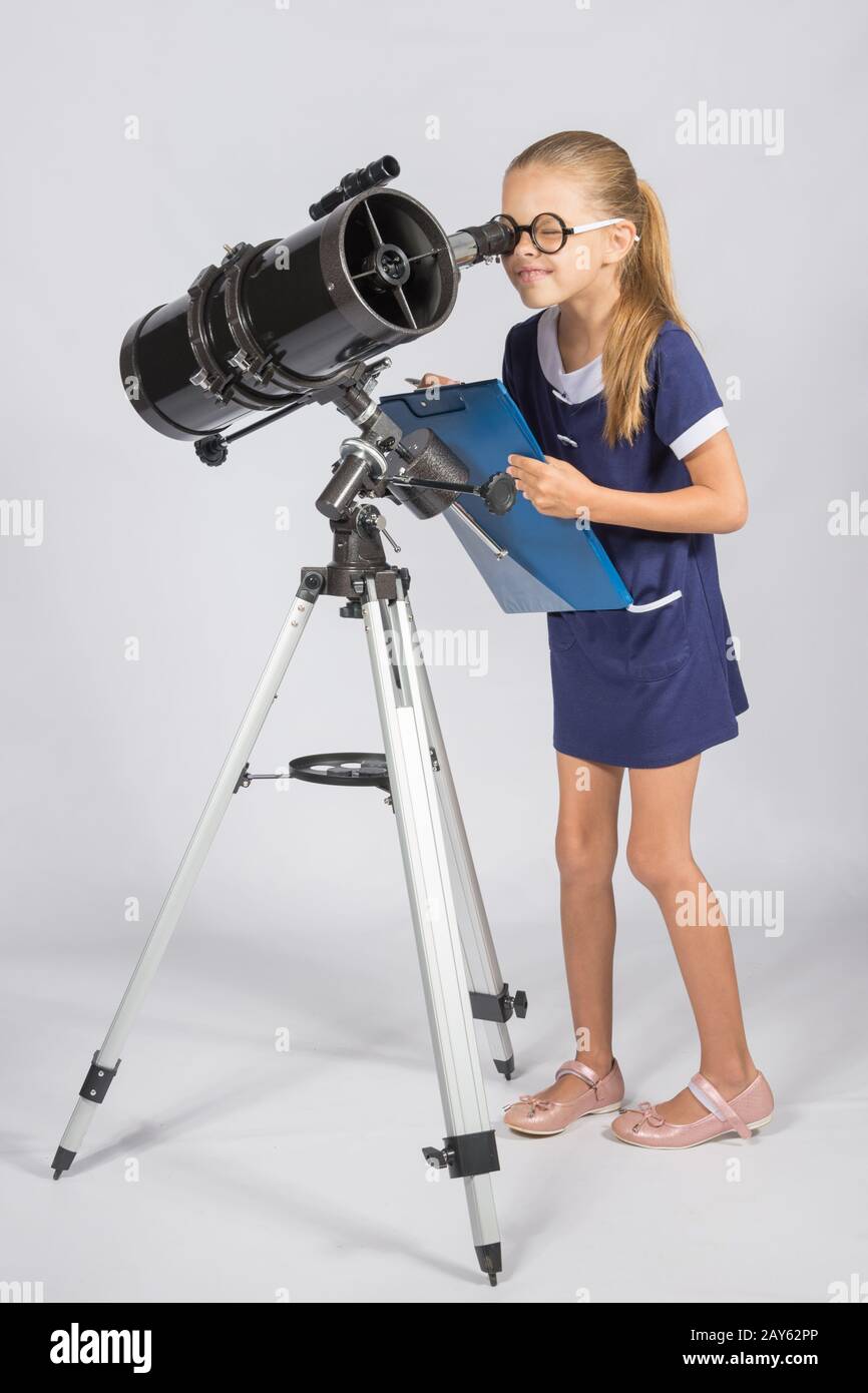 El joven astrónomo en vidrios con interés sus compañeros en el ocular del telescopio Foto de stock
