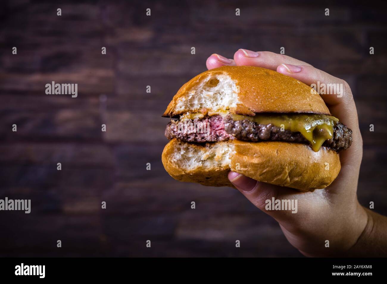A mano sosteniendo una burger de carne artesanal con queso sobre fondo  rústico Fotografía de stock - Alamy