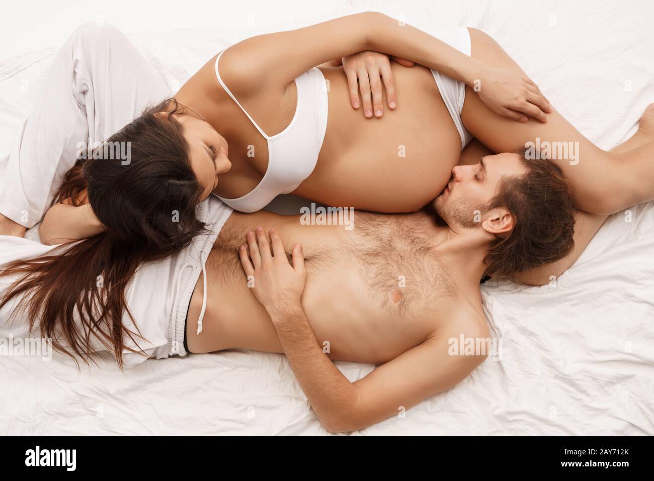 Hombre bese barriga de embarazada esposa acostada en la cama Foto de stock