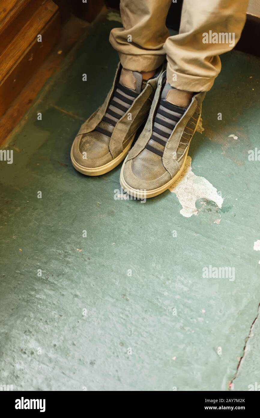 Las piernas de un niño en pantalones caqui y zapatillas de deporte de pie en la puerta de la habitación Foto de stock